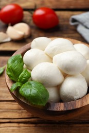 Photo of Delicious mozzarella balls and basil leaves in bowl on wooden table, closeup