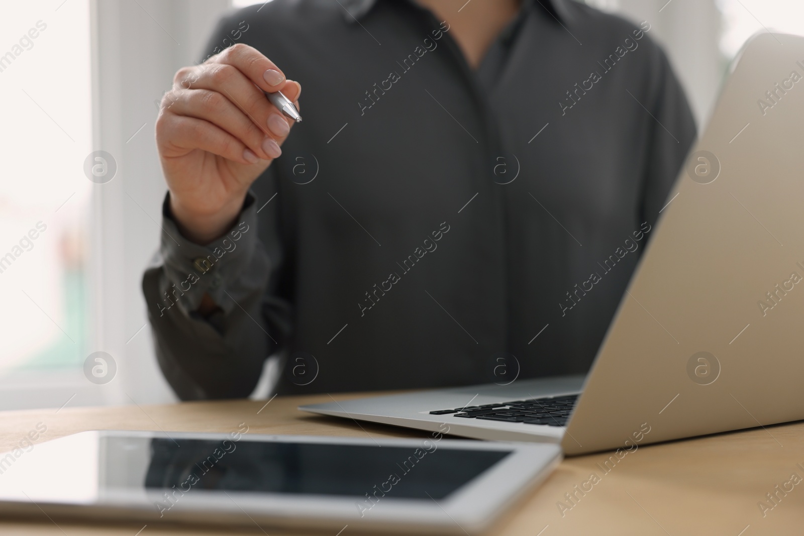 Photo of Woman with tablet and pen working on laptop at wooden table, closeup. Electronic document management