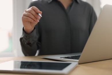 Woman with tablet and pen working on laptop at wooden table, closeup. Electronic document management