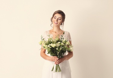 Young bride wearing wedding dress with beautiful bouquet on beige background