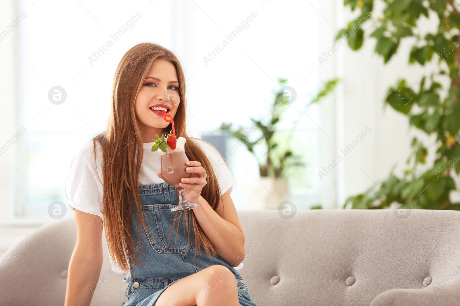 Photo of Young woman with glass of delicious milk shake indoors
