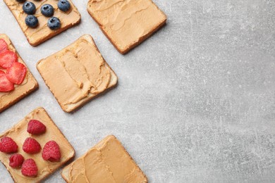 Photo of Tasty peanut butter sandwiches with fresh berries on gray table, flat lay. Space for text