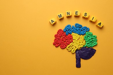 Photo of Cubes with word Amnesia and human brain made of colorful plasticine on orange background, flat lay. Space for text