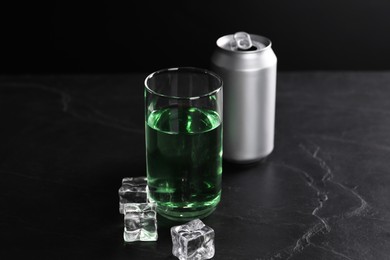 Photo of Energy drink in glass, aluminium can and ice cubes on black table