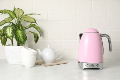 Photo of Modern electric kettle, houseplant and tea set on counter in kitchen