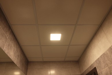 Photo of Ceiling with PVC tiles and lighting indoors, low angle view