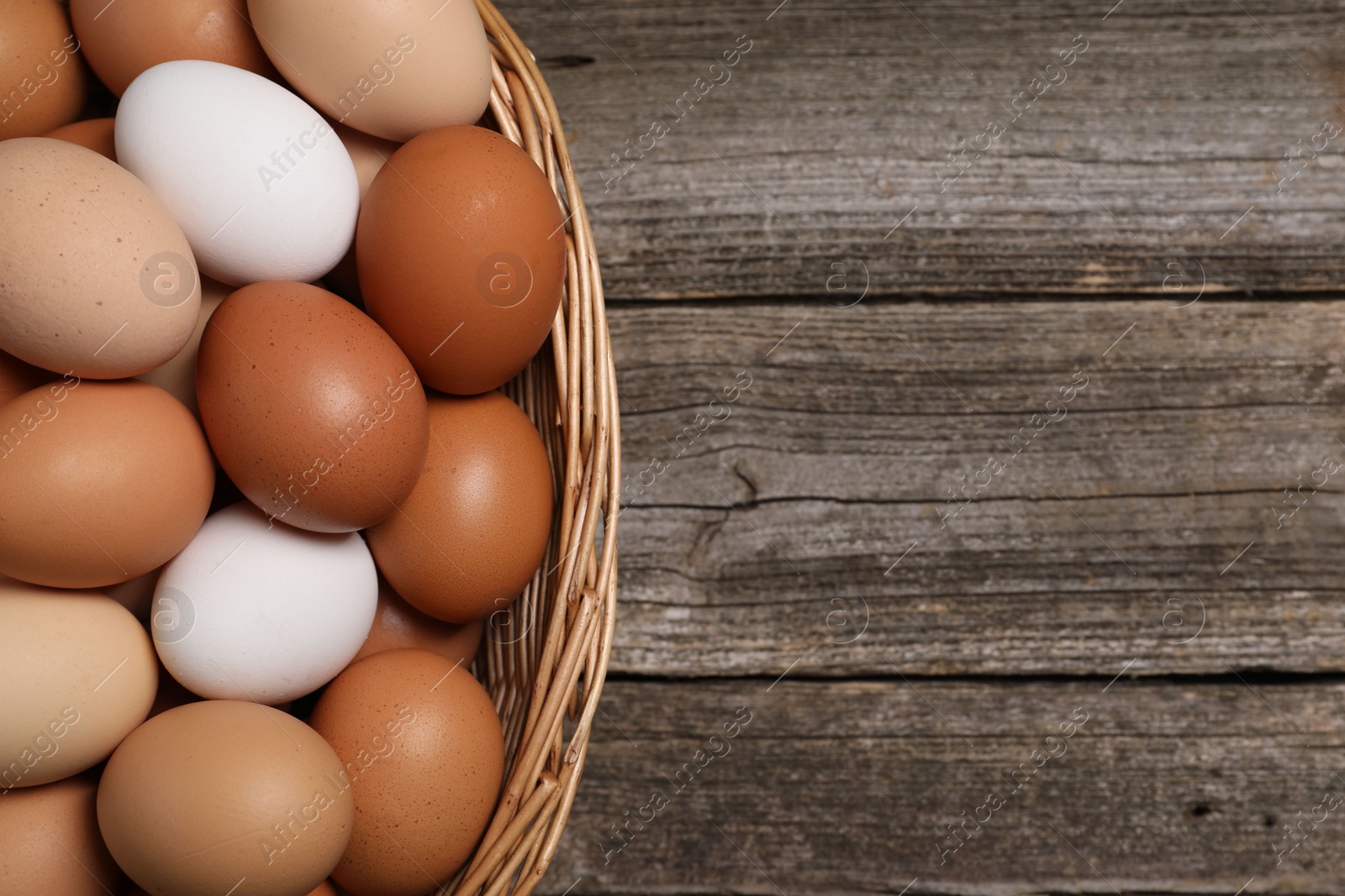 Photo of Fresh chicken eggs in wicker basket on wooden table, top view. Space for text