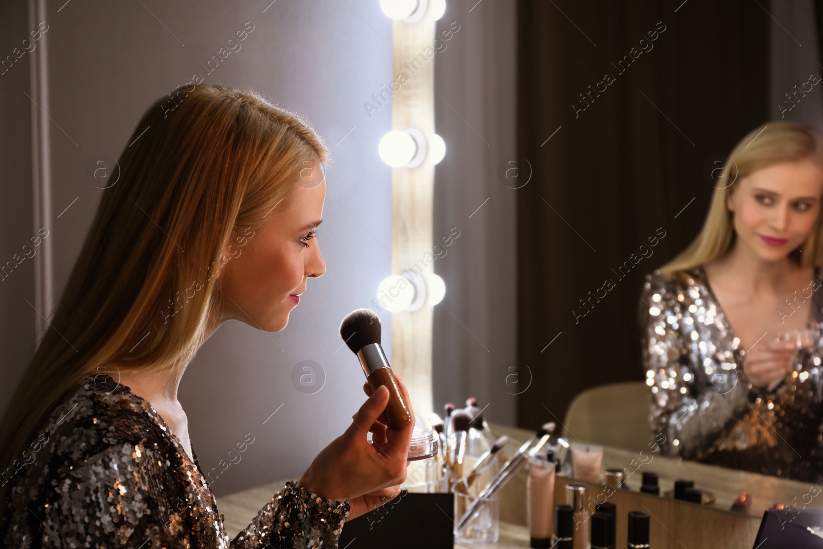 Photo of Beautiful woman applying makeup near mirror in room