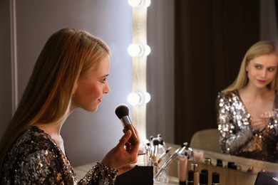 Beautiful woman applying makeup near mirror in room