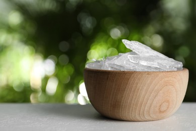 Photo of Menthol crystals in wooden bowl on white table against blurred background. Space for text
