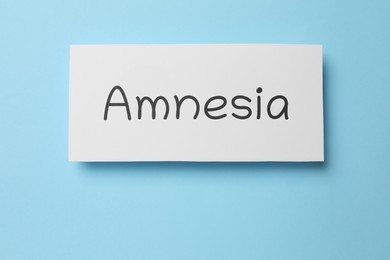 Photo of Card with word Amnesia on light blue background, top view