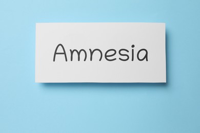 Card with word Amnesia on light blue background, top view