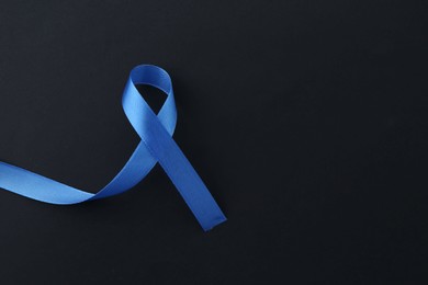 Blue awareness ribbon on black background, top view. Space for text