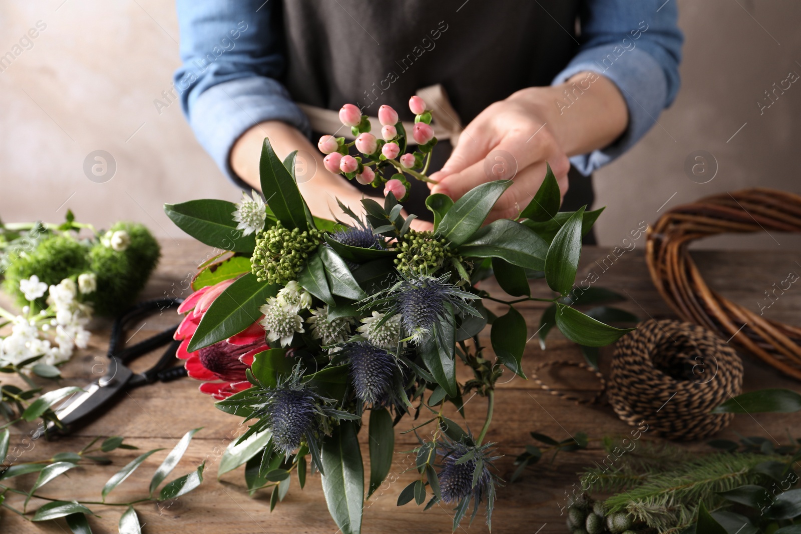 Photo of Florist making beautiful bouquet with fresh flowers at wooden table, closeup