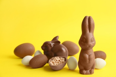 Photo of Chocolate Easter bunnies, eggs and candies on yellow background. Space for text