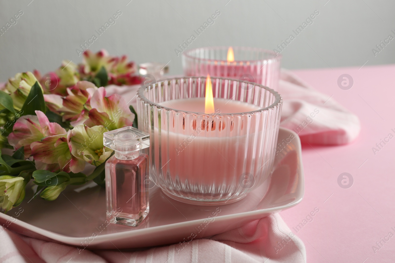 Photo of Stylish tender composition with burning candles and flowers on pink table. Cozy interior element