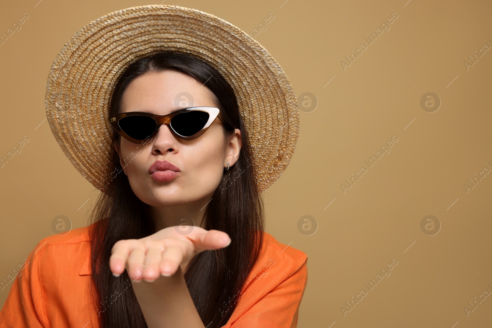 Photo of Beautiful young woman in straw hat blowing kiss on beige background. Space for text