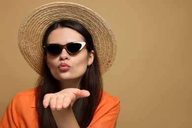 Beautiful young woman in straw hat blowing kiss on beige background. Space for text