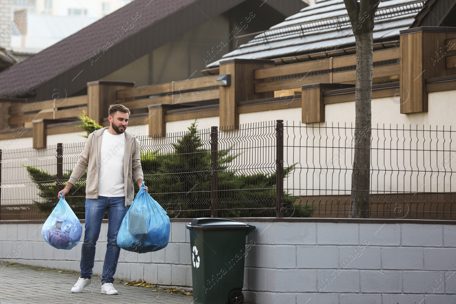 Photo of Man carrying garbage bags to recycling bin outdoors