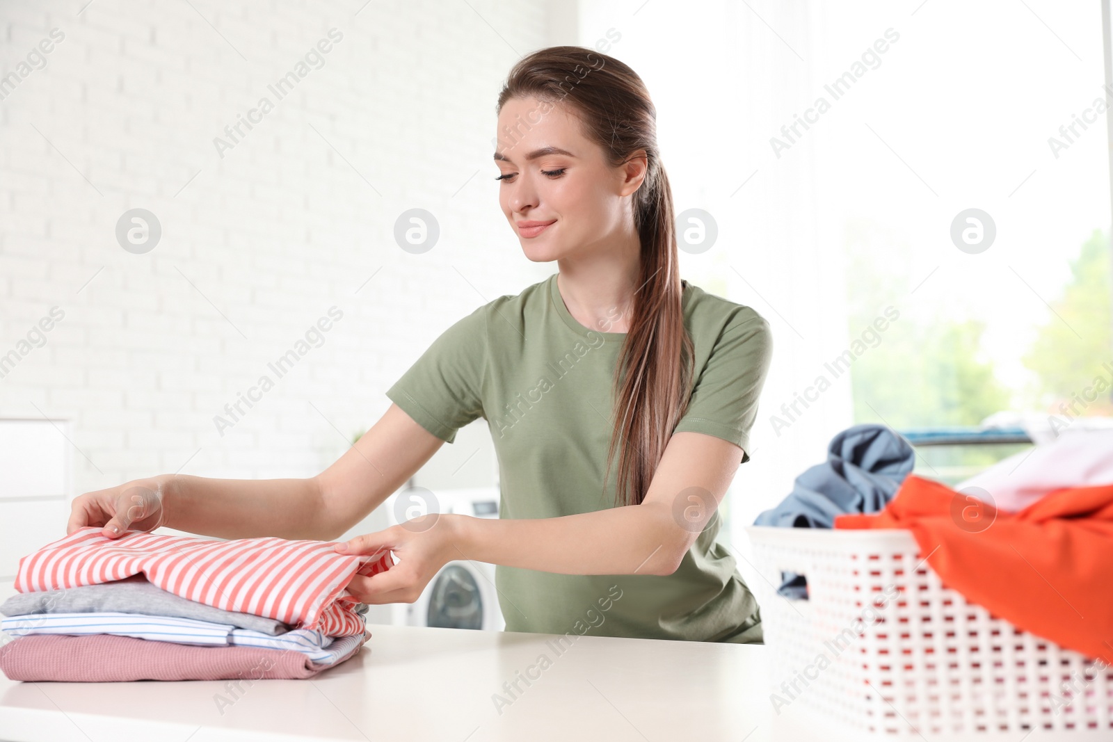 Photo of Happy woman with clean laundry at table indoors