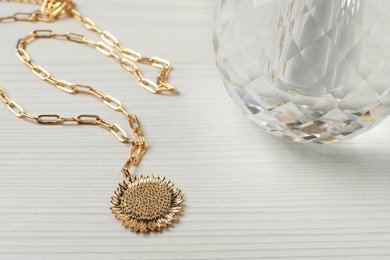 Necklace and bottle of perfume on white wooden table, closeup