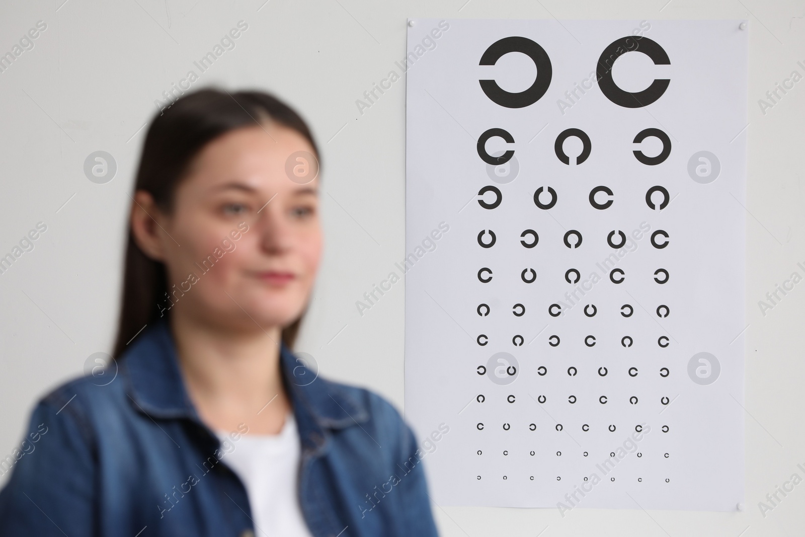 Photo of Young woman against vision test chart, selective focus