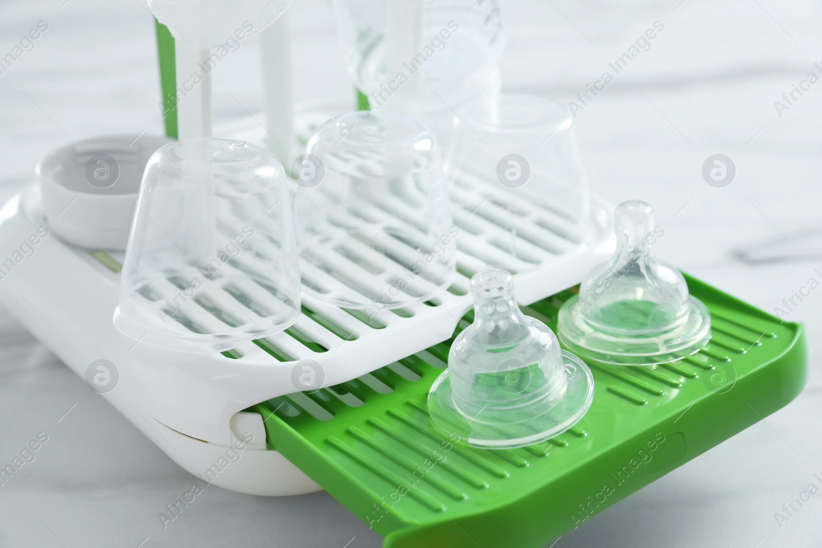 Photo of Dryer with baby bottles and nipples after sterilization on white marble table in kitchen, closeup