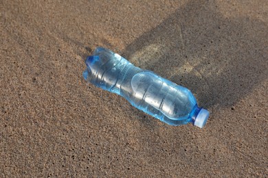 Photo of Plastic bottle of fresh water on wet sand, above view