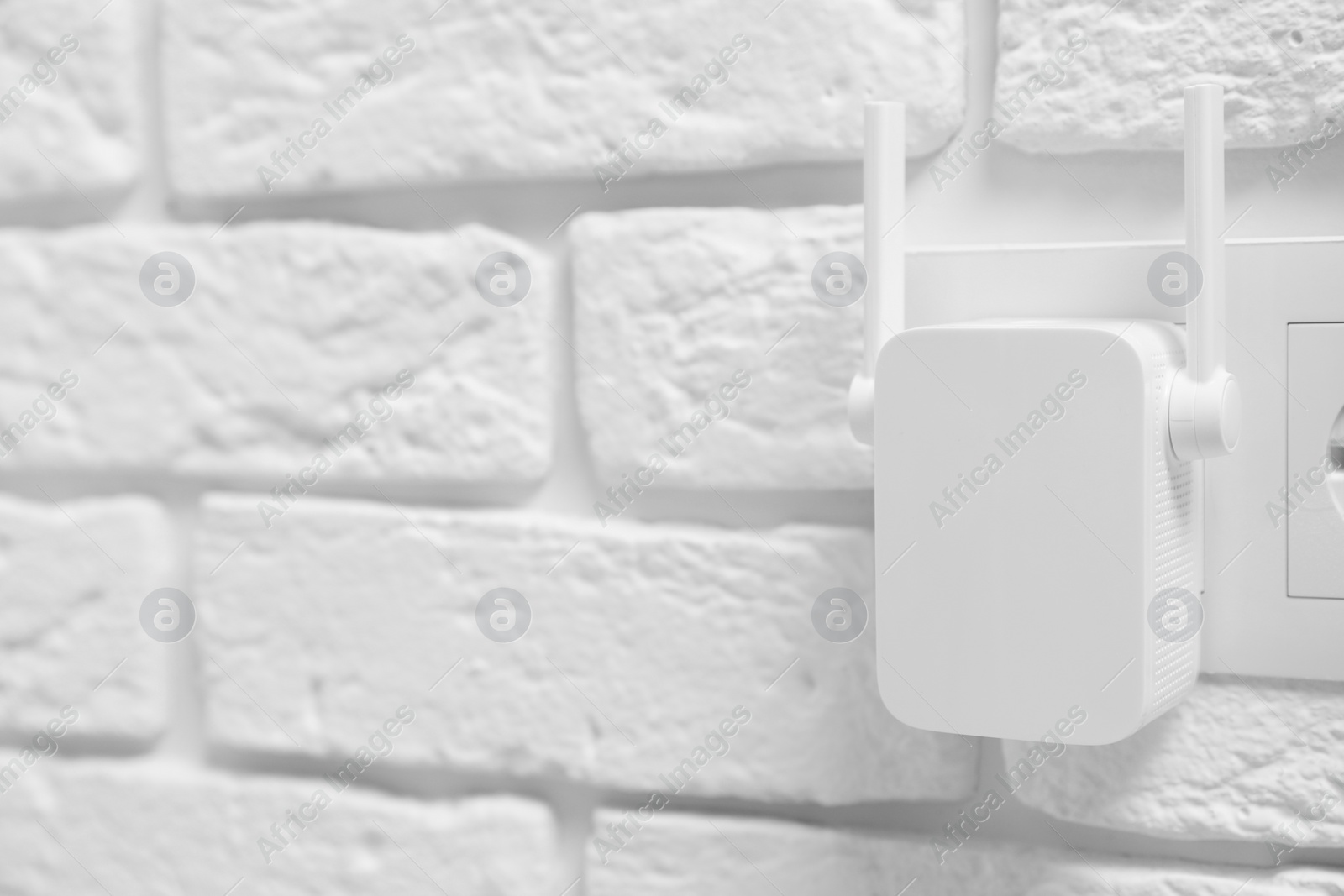 Photo of Wireless Wi-Fi repeater on white brick wall, space for text