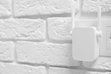 Wireless Wi-Fi repeater on white brick wall, space for text