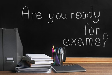 Photo of Different stationery on wooden table near blackboard with phrase Are You Ready For Exams