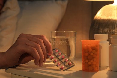 Photo of Woman taking pills from nightstand indoors, closeup. Insomnia treatment