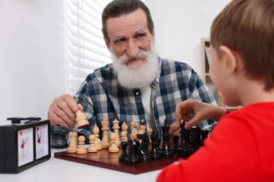 Photo of Grandfather and grandson playing chess at table in room