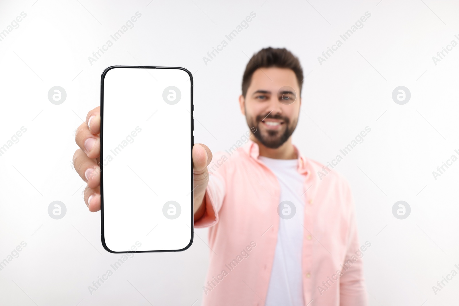 Photo of Young man showing smartphone in hand on white background, selective focus. Mockup for design