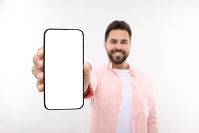 Photo of Young man showing smartphone in hand on white background, selective focus. Mockup for design