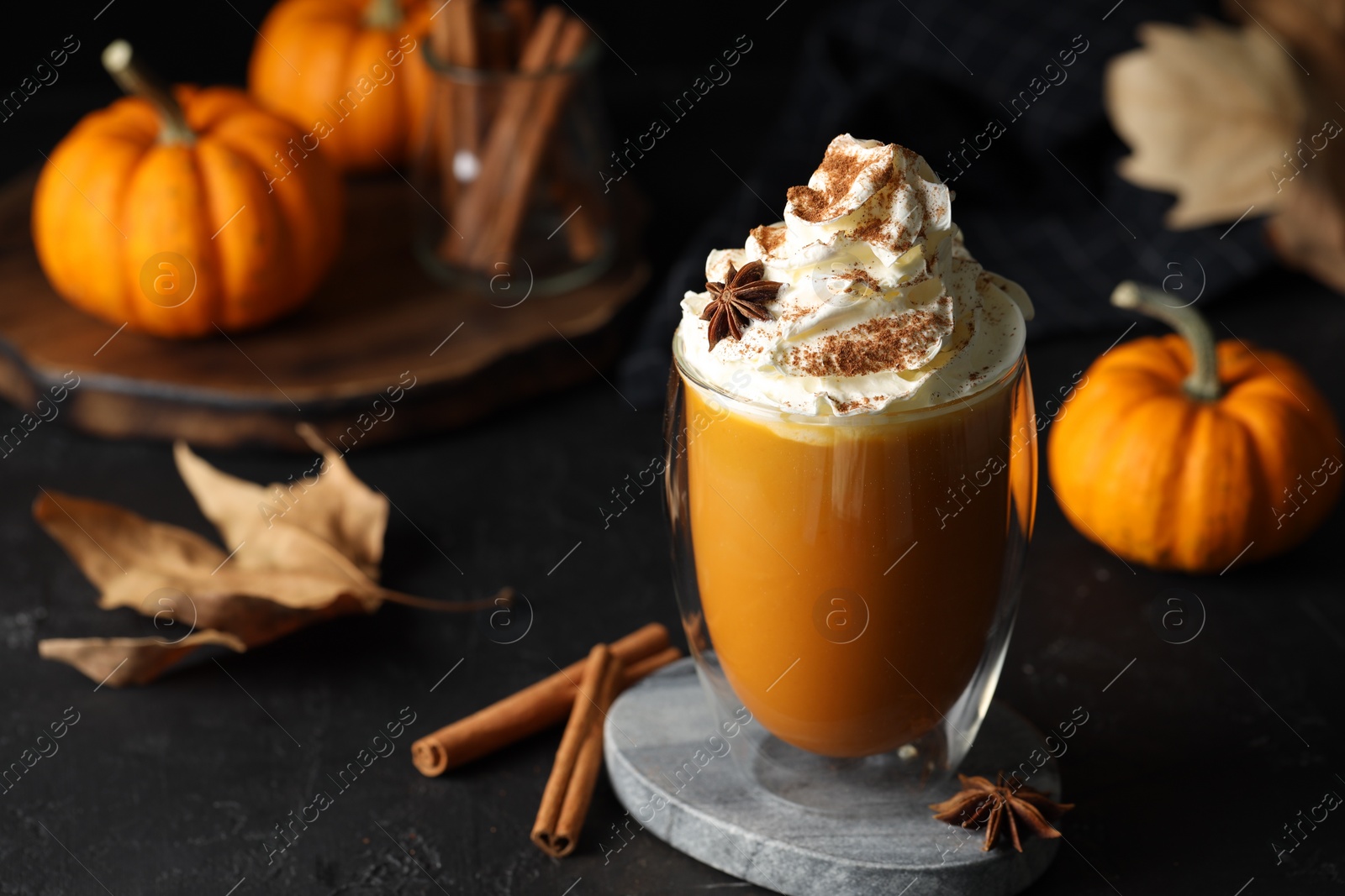 Photo of Glass of pumpkin spice latte with whipped cream and ingredients on black table