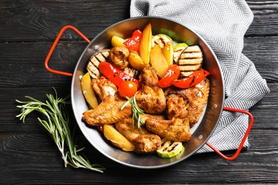 Photo of Wok with barbecued chicken wings and garnish on wooden background, top view