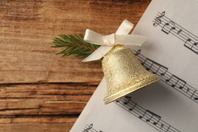 Photo of Golden shiny bell with bow and music sheet on wooden table, flat lay. Space for text. Christmas decoration