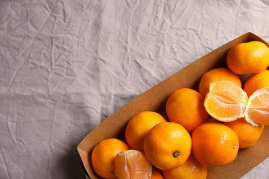 Photo of Paper box with fresh ripe tangerines on beige cloth, top view. Space for text