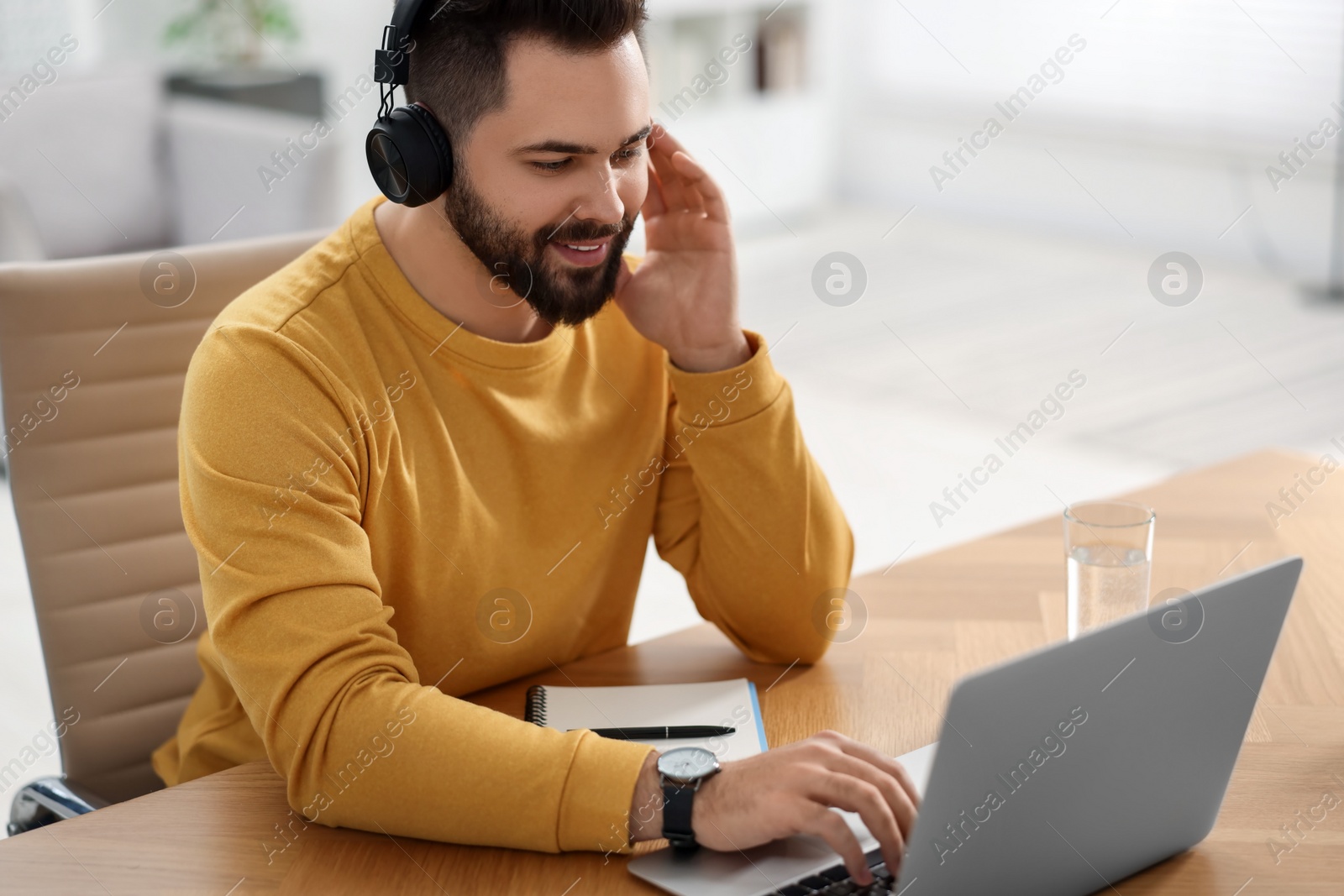 Photo of Young man in headphones watching webinar at table in room