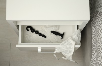 Photo of Black anal plug, beads and women's underwear in open drawer of bedside table indoors, above view. Sex toys