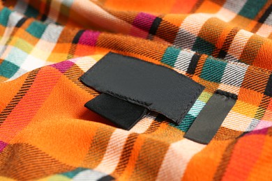 Photo of Blank clothing label on checkered apparel, closeup
