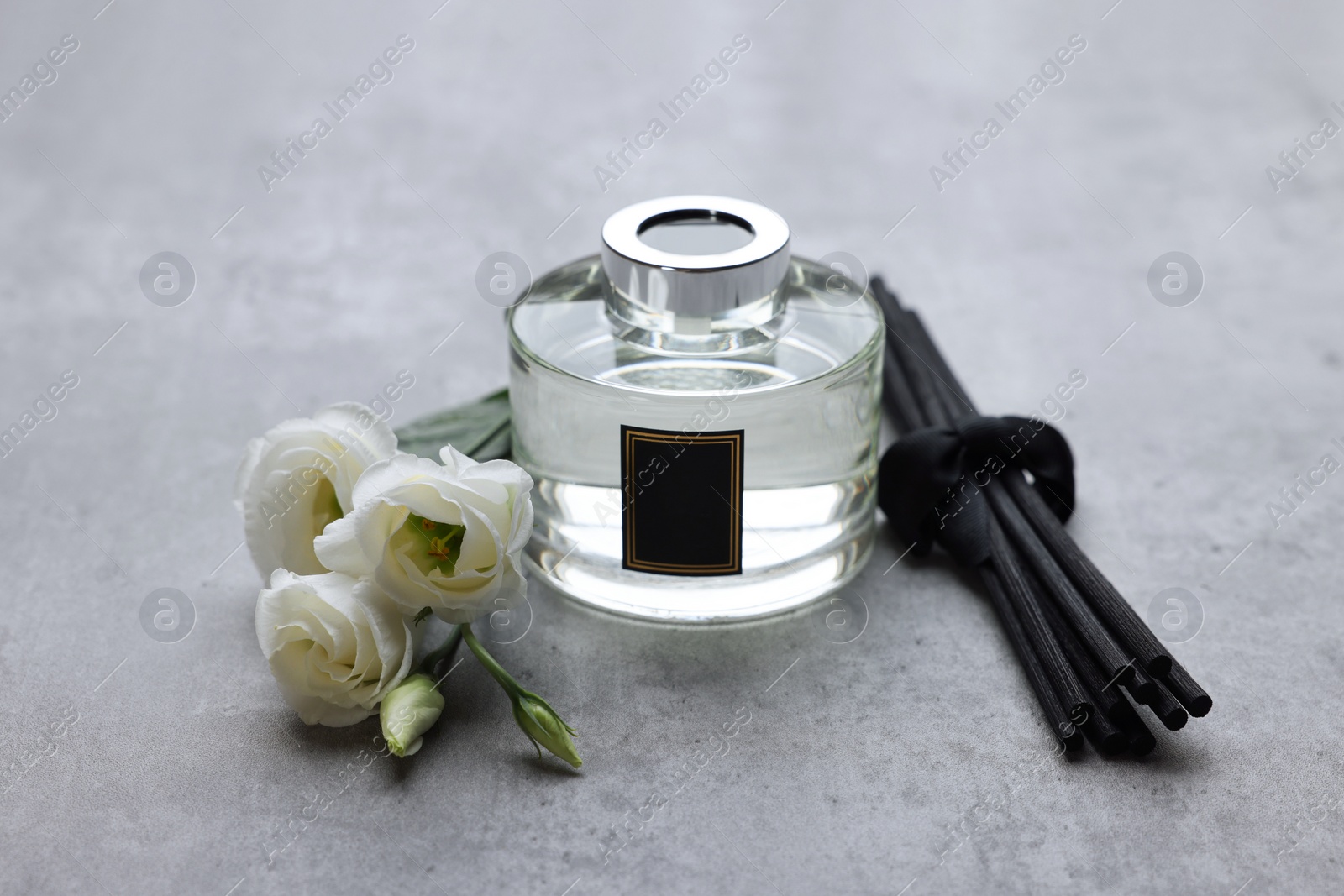 Photo of Reed sticks, glass bottle with aromatic liquid and eustoma flowers on gray marble table