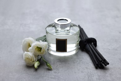 Reed sticks, glass bottle with aromatic liquid and eustoma flowers on gray marble table