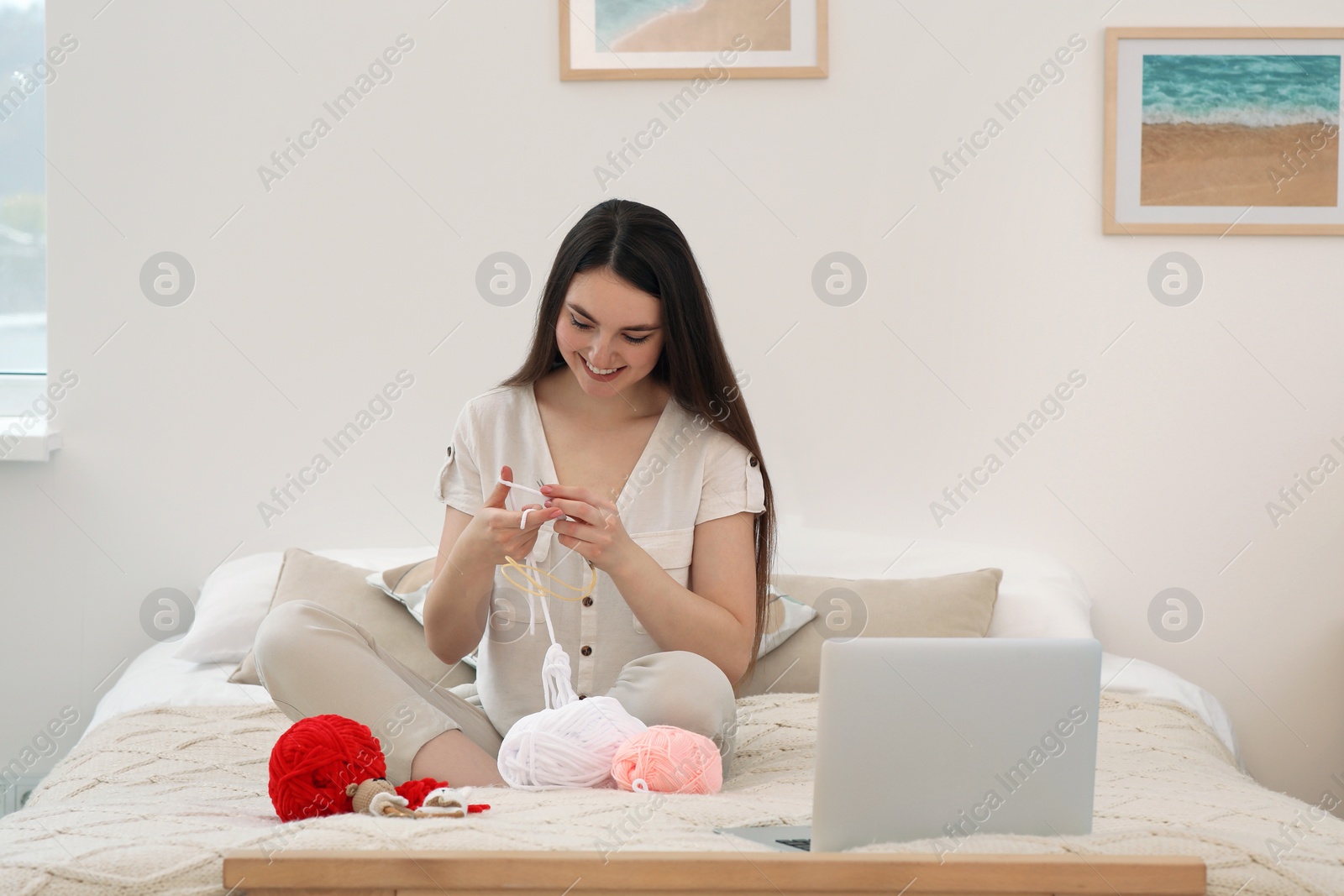 Photo of Young woman learning to knit with online course at home. Handicraft hobby