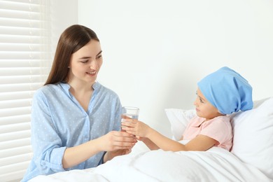 Photo of Childhood cancer. Mother giving daughter glasswater in hospital