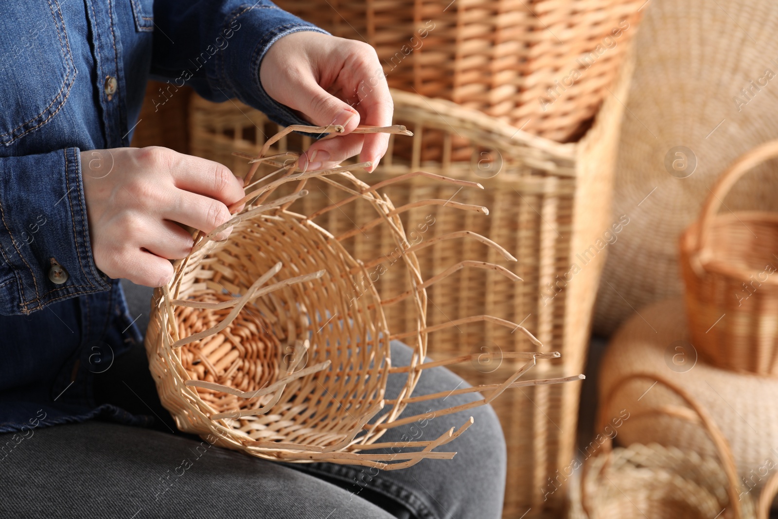 Photo of Woman weaving wicker basket indoors, closeup view