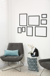 Photo of Stylish room interior with empty frames hanging on white wall and comfortable furniture