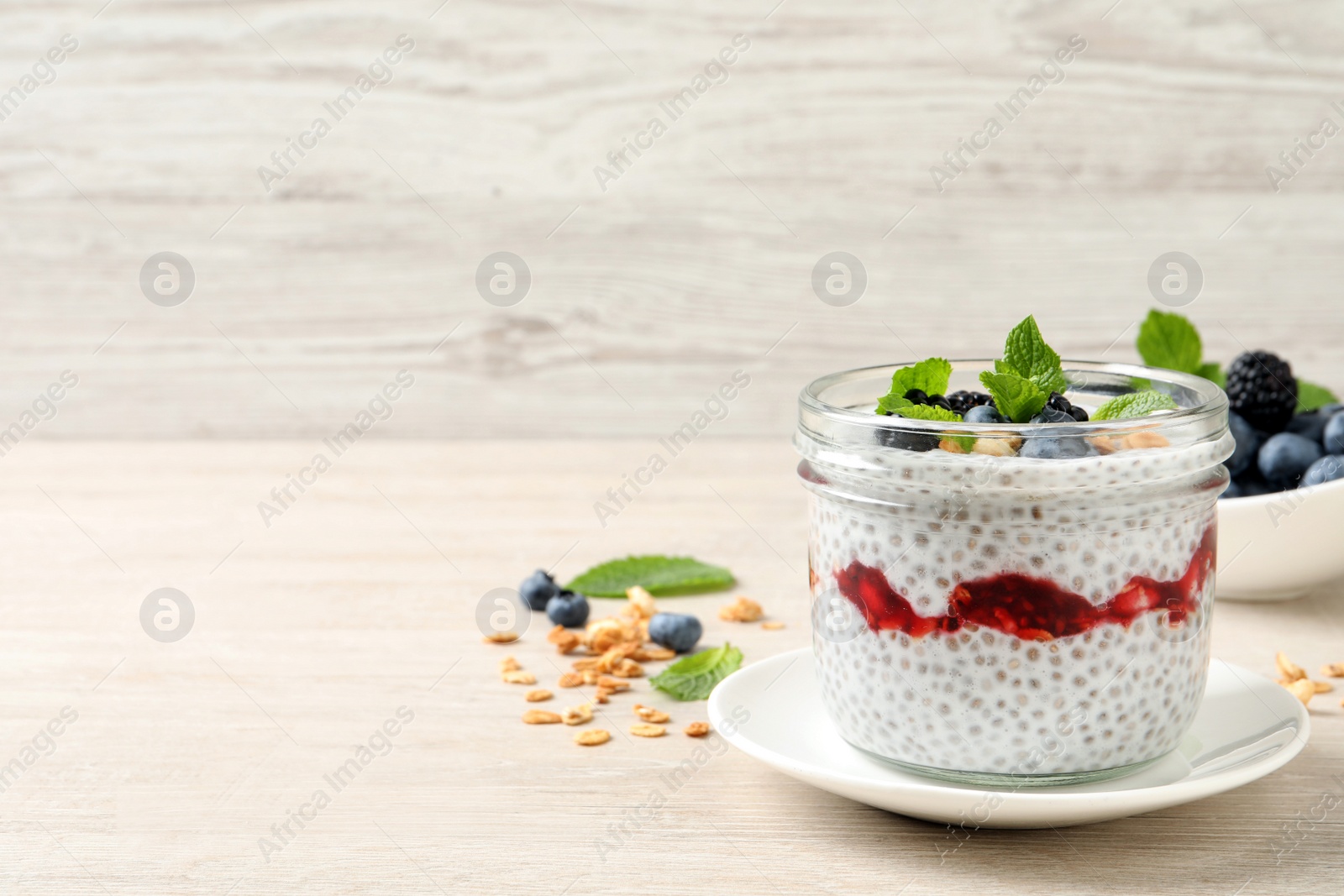 Photo of Delicious chia pudding with berries and granola on wooden table. Space for text