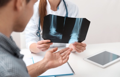 Photo of Orthopedist showing X-ray picture to patient at table in clinic, closeup